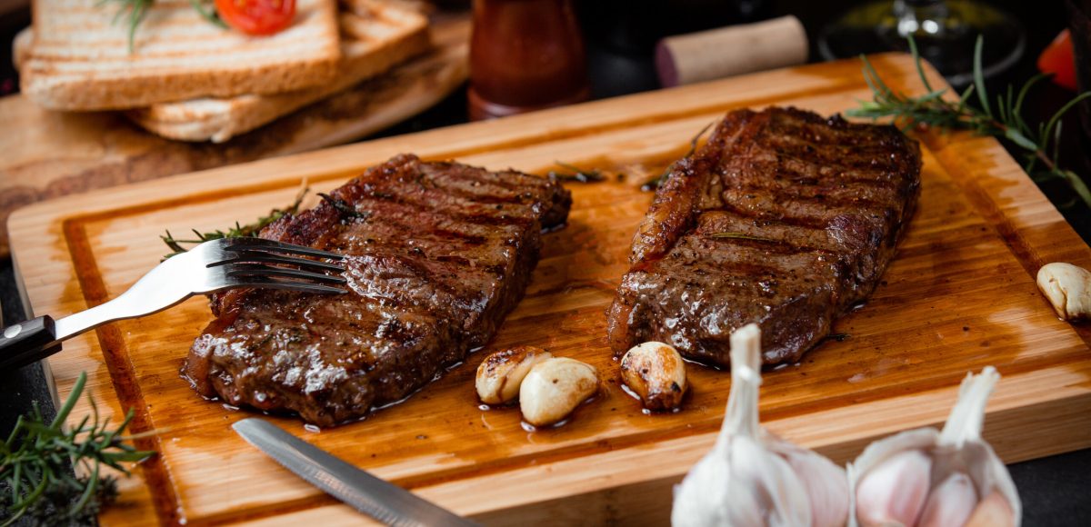 fried steak pieces on a wooden board and garlic